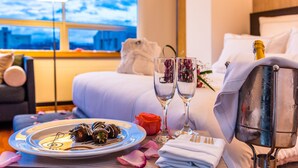 A hotel room with a bed, a bedside table with a champagne bottle, two glasses, a plate of food, and a rose. - One Sixteen Hotel (Bogotá)