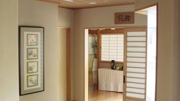 A hallway with a wooden floor, a framed picture on the wall, and a sliding door leading to a room with a tatami mat and a small table.
