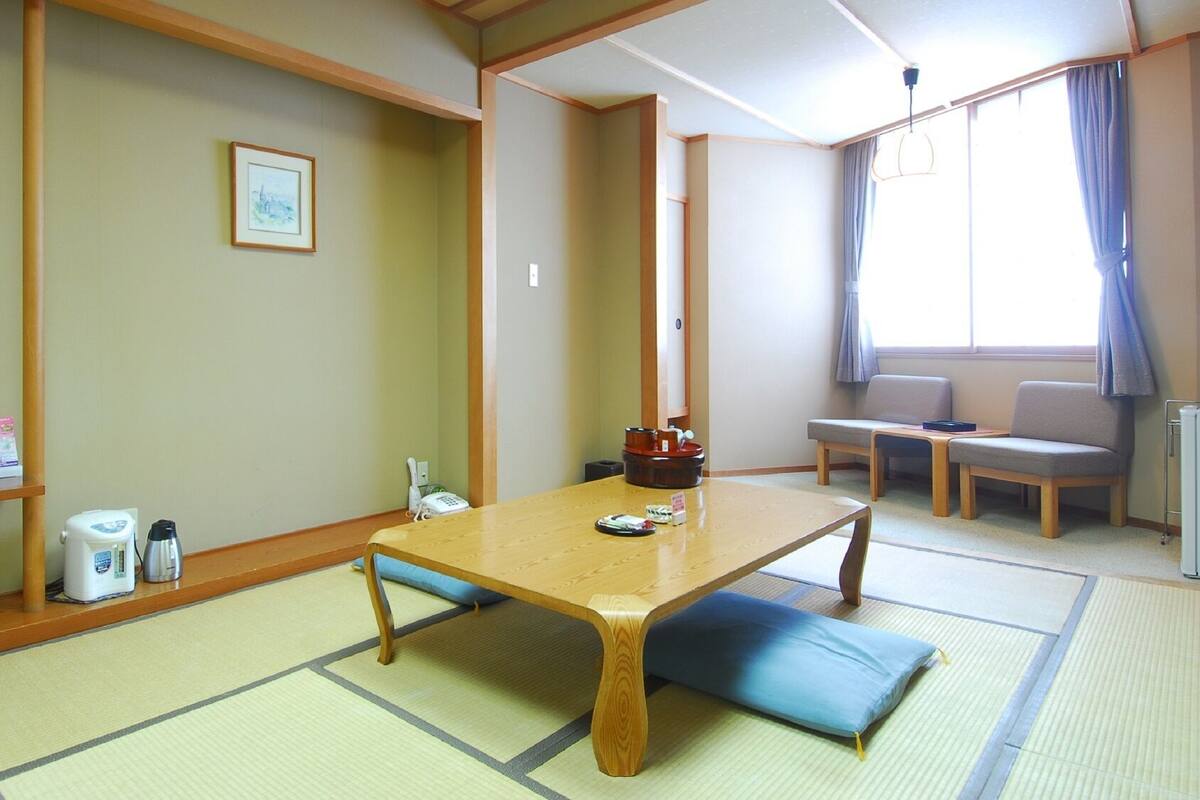 A traditional Japanese room with tatami flooring, a low wooden table, a cushioned bench, and a small shelf with toiletries.