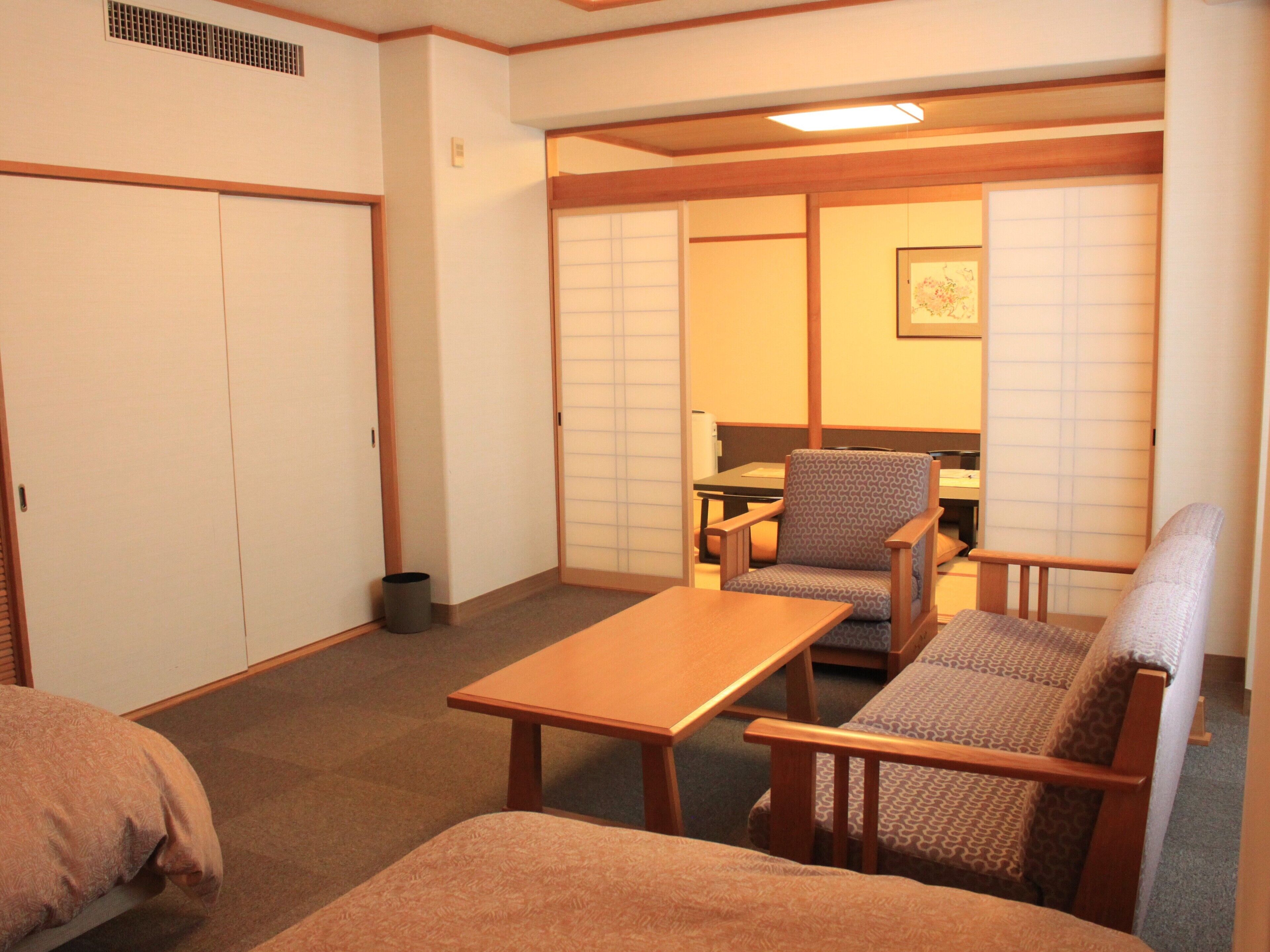 A traditional Japanese-style room with tatami flooring, a low table, two patterned chairs, and a sliding shoji screen door.