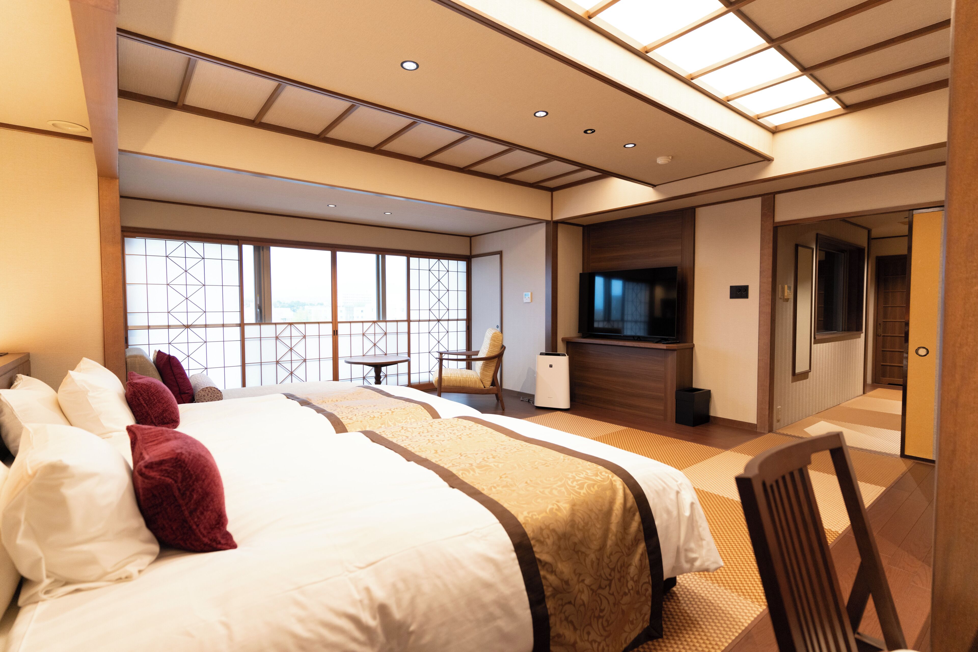 A hotel room with a large bed, a TV, a desk, and a view through a window.