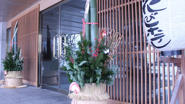 Fachada de edificio con un amplio acceso de vidrio, listones verticales de madera y un árbol navideño decorativo con base de tejido.