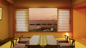 Una habitación japonesa tradicional con suelo de tatami, una mesa baja con cojines y vistas a través de biombos shoji.