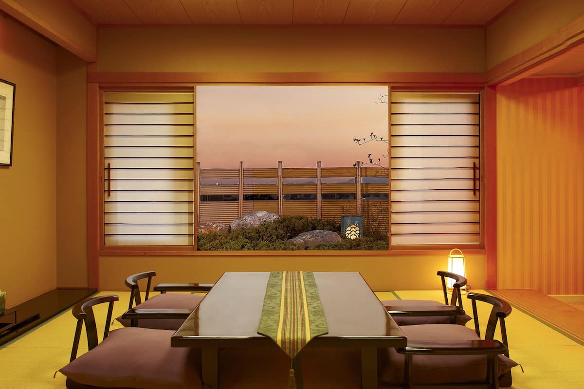 A traditional Japanese room with tatami flooring, a low table with cushions, and a view through shoji screens.
