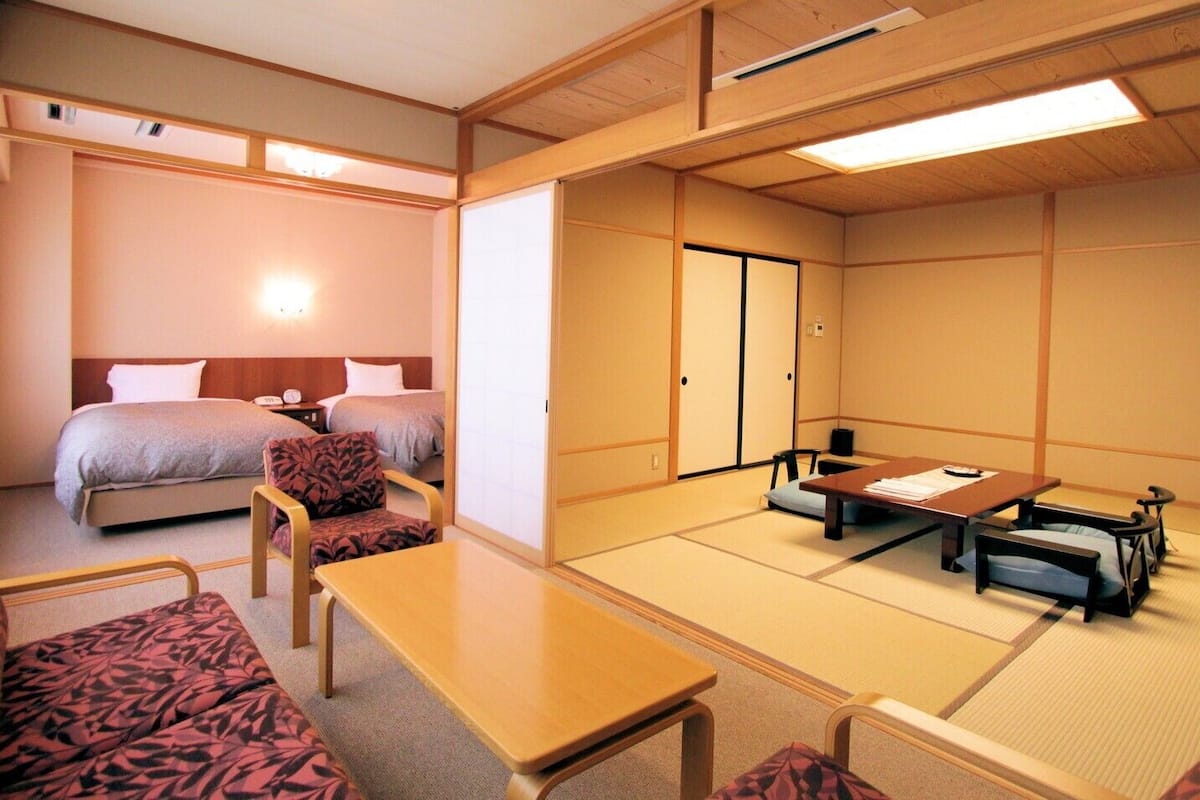 A traditional Japanese room with tatami flooring, a low table, a sofa, and two beds.