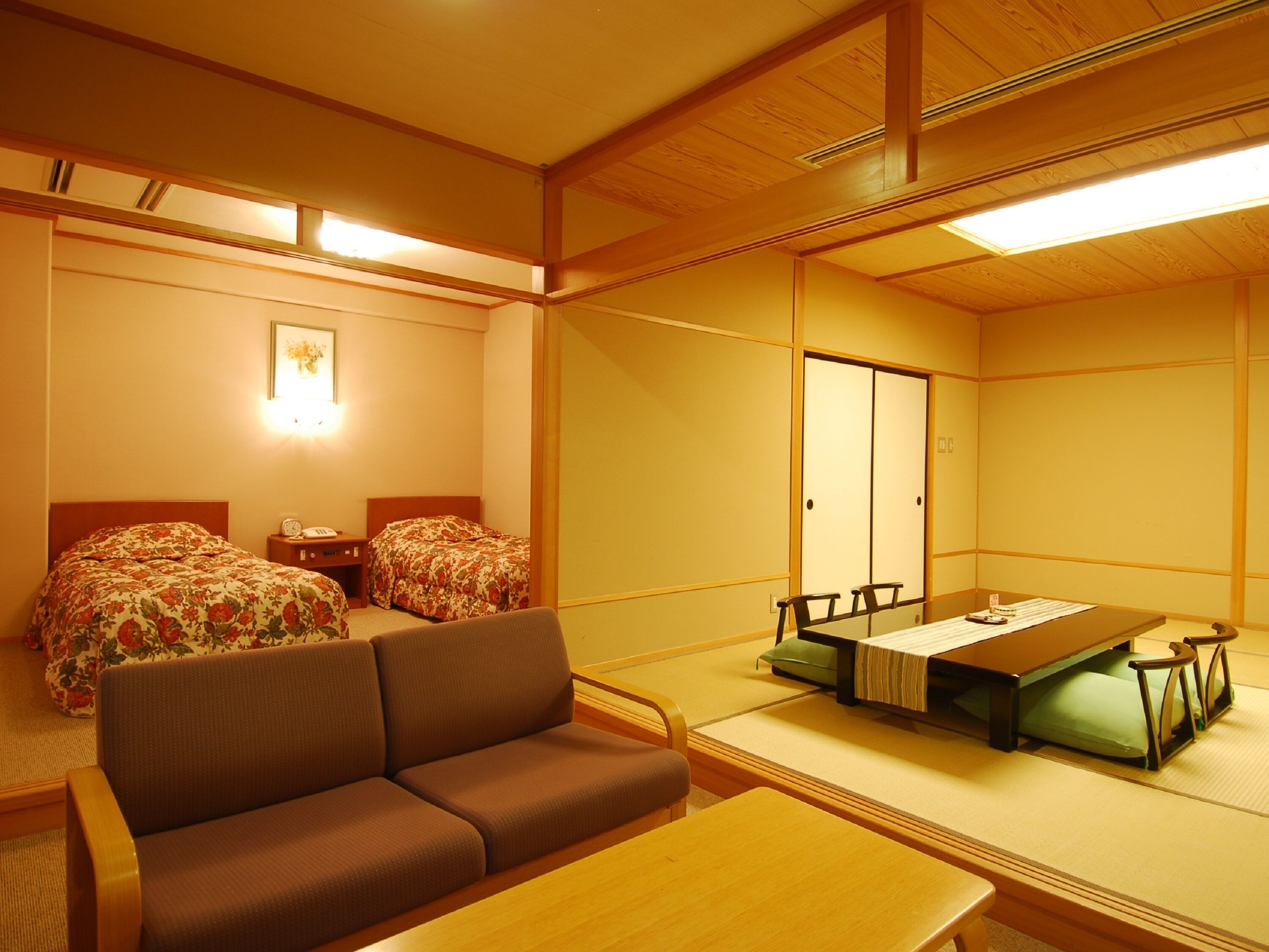 Une pièce de style japonais traditionnel, avec un sol recouvert de tatamis, une table basse, un canapé et deux lits dotés de draps à motifs floraux.