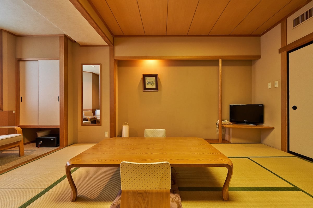 A traditional Japanese room with tatami flooring, a low table, a chair, a television, and a wardrobe.