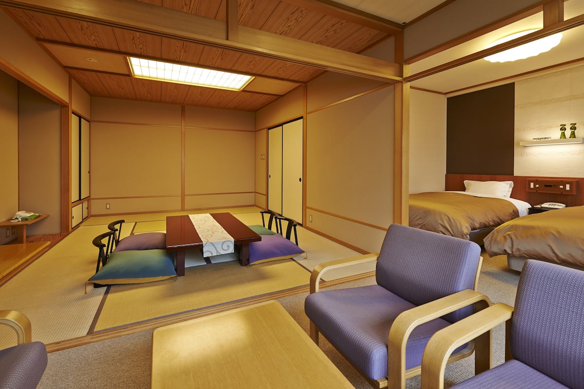 A traditional Japanese-style room with tatami flooring, a low wooden ceiling, and a bed with a wooden headboard.