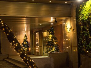 A building entrance with two Christmas trees decorated with lights, a staircase, and a sign with Japanese characters. - Hanabishi Hotel (Hakodate)