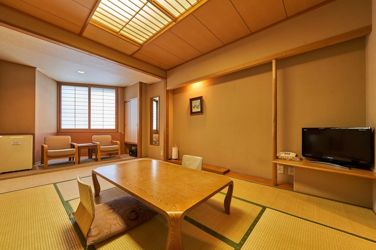 A traditional Japanese-style room with tatami flooring, a low table, and a television on a stand.