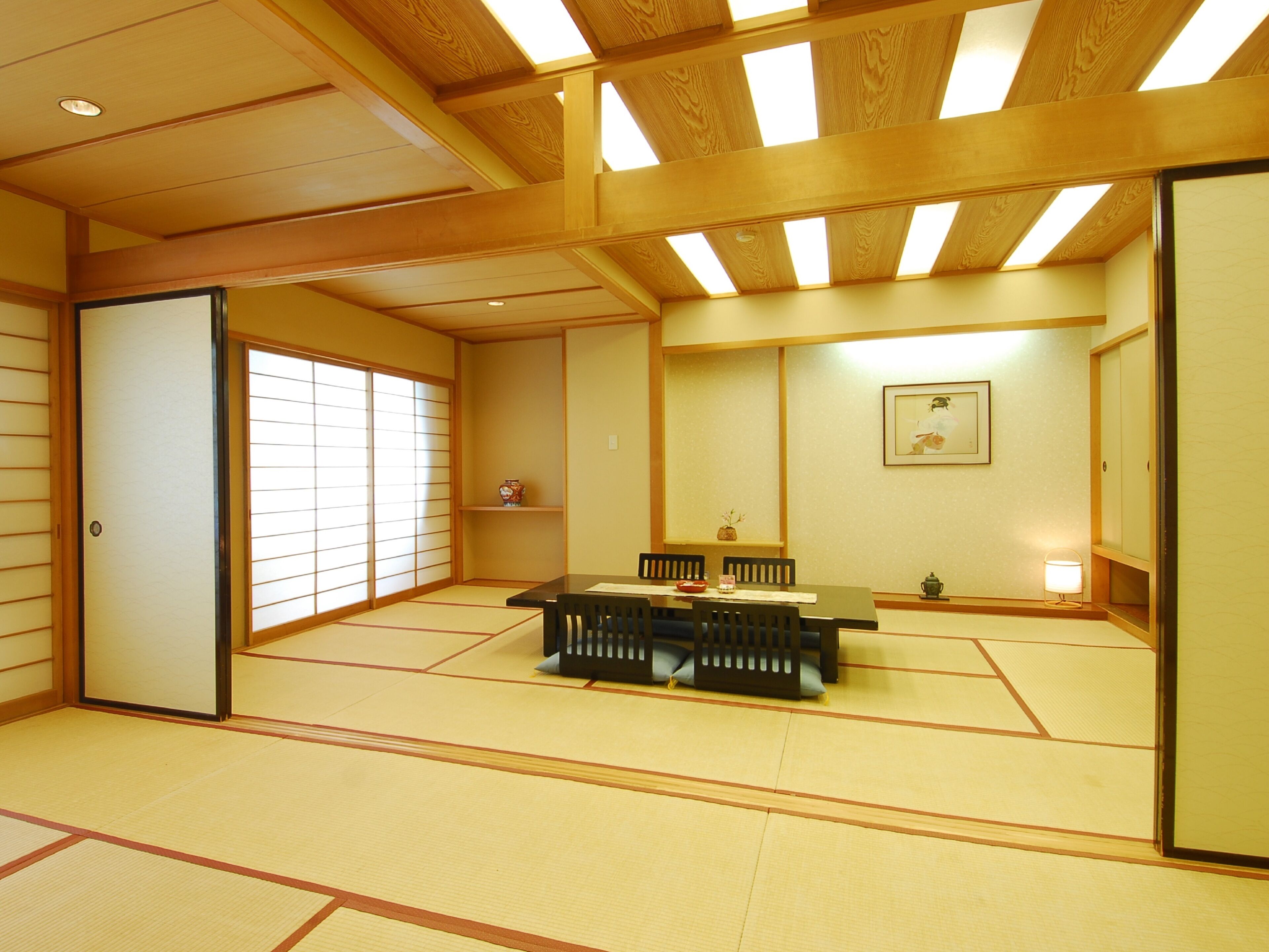 Une pièce de style japonais traditionnel, avec un sol recouvert de tatamis, une table basse entourée de chaises, une porte coulissante et un tableau accroché au mur.