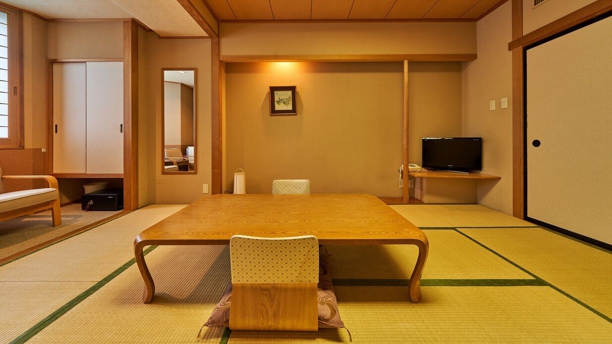 A traditional Japanese room with tatami flooring, a low table, a chair, a television, and a sliding door.