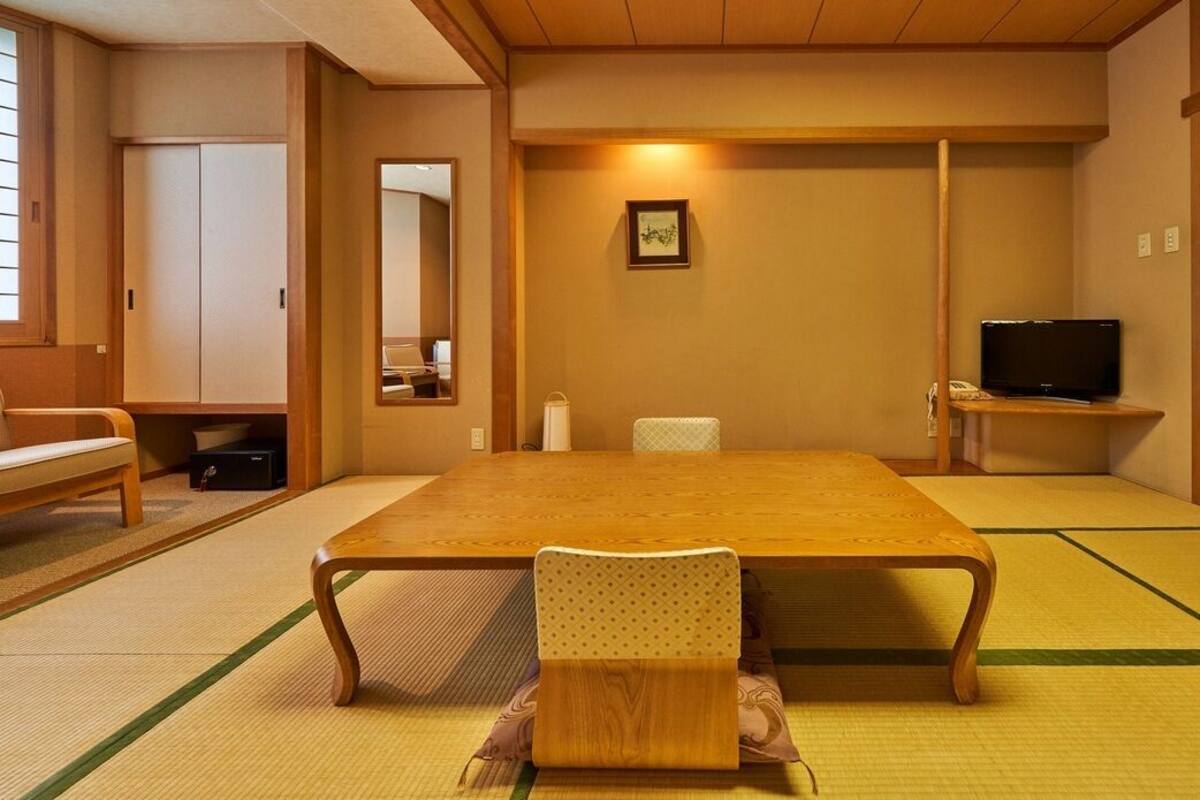 A traditional Japanese room with tatami flooring, a low table, a chair, a television, and a sliding door.