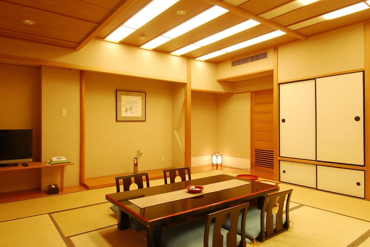 A traditional Japanese-style room with tatami flooring, a low table with chairs, a television, and a sliding door.