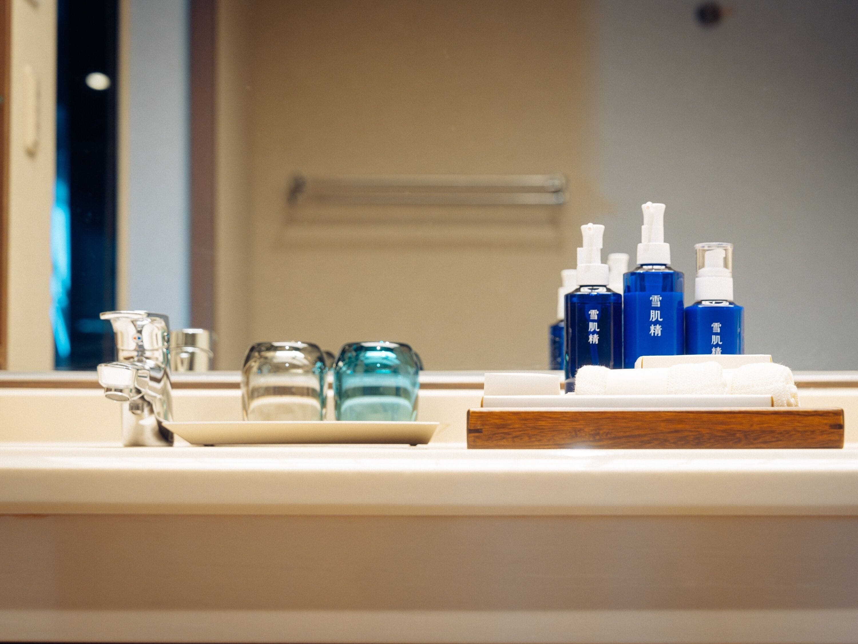 A bathroom sink with a mirror, a faucet, and a tray holding blue bottles and a white towel.