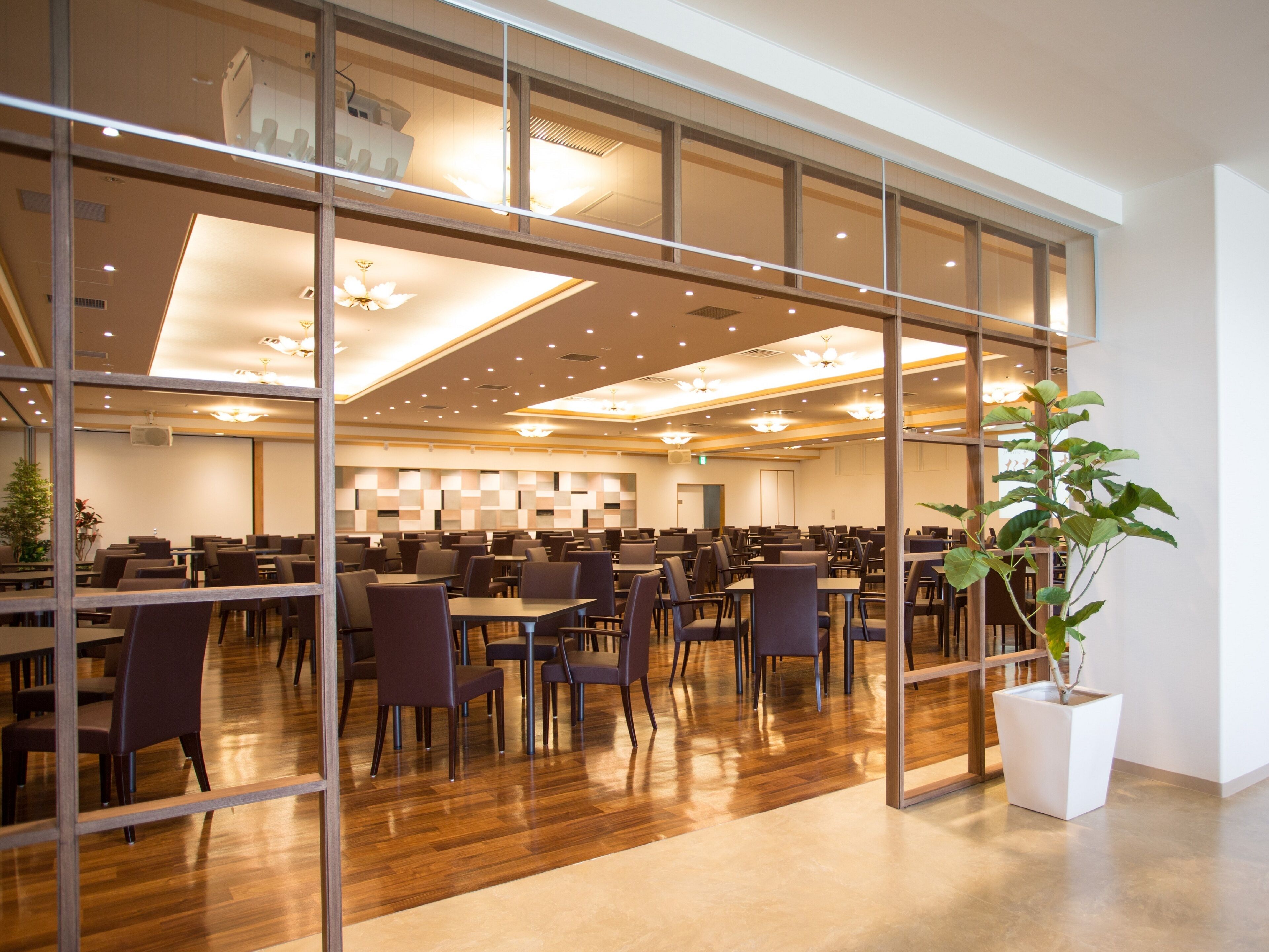 Un'ampia sala da pranzo con diversi tavoli e sedie, una grande pianta in vaso e un moderno design del soffitto.