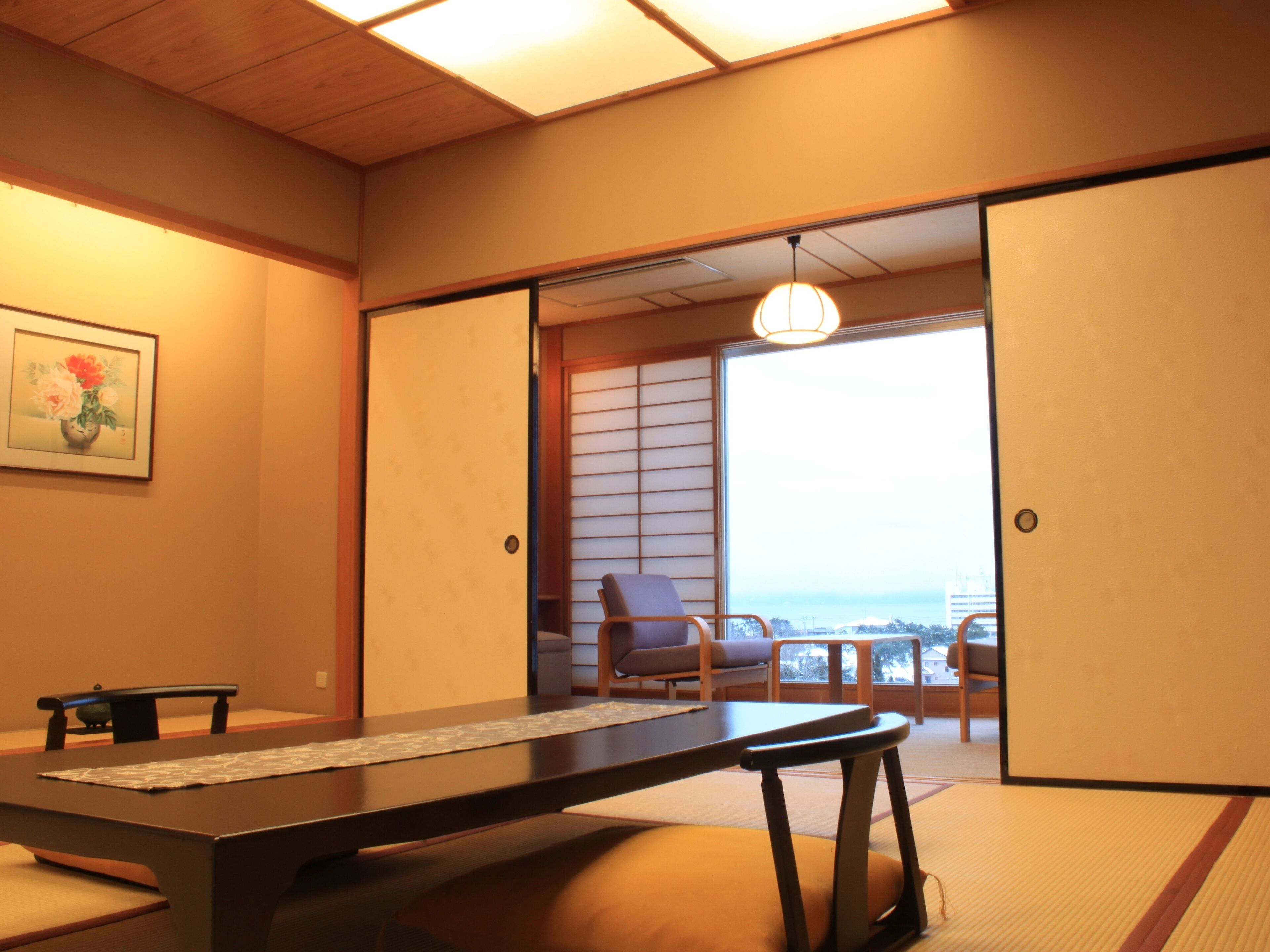 Una habitación japonesa tradicional con suelo de tatami, una mesa baja y puertas correderas que dan a un balcón con vistas.
