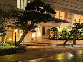 Edificio japonés tradicional con entrada de madera, sendero de piedra y jardín cuidado.