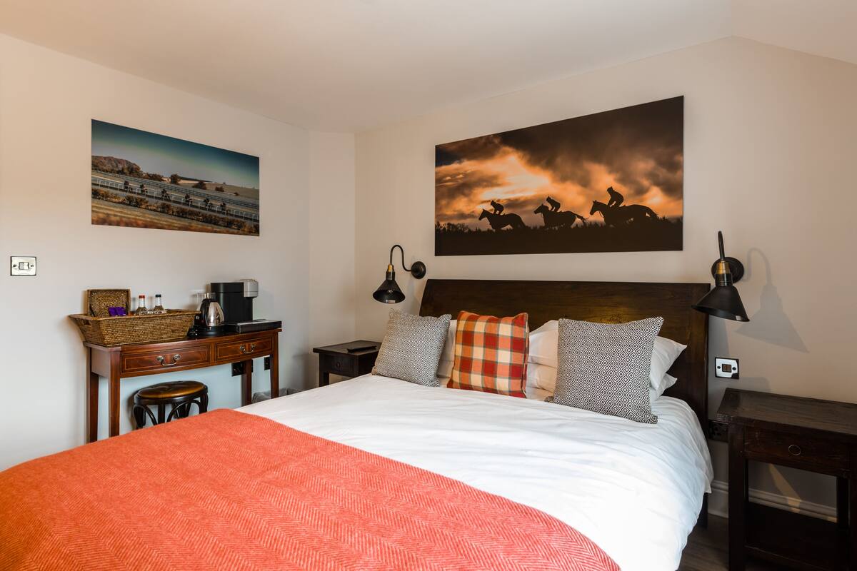 Quarto de hotel bem arrumado com uma cama grande, uma escrivaninha com cafeteira e duas luminárias de parede.