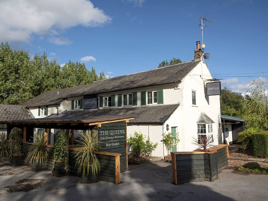A white building with green shutters, labeled "The Queens Pub Dining & Bedrooms Beer Garden."