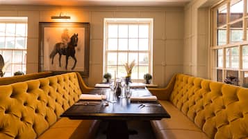 Un comedor con una mesa larga, asientos tipo cabina tapizados en amarillo y un cuadro enmarcado de un caballo en la pared.