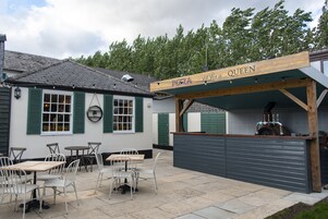 Un restaurante llamado "Pizza Queen" con mesas al aire libre y una barra.