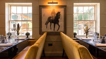 Un comedor con una mesa larga, bancos acolchados y una obra de arte enmarcada de un caballo en la pared.