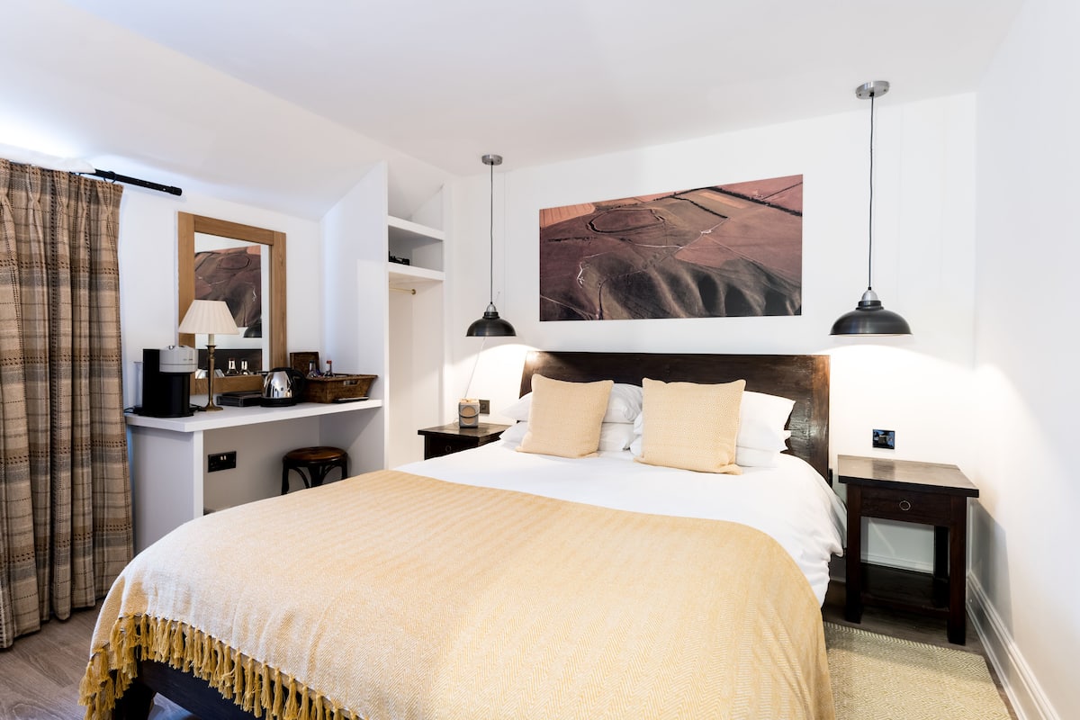 Quarto bem arrumado com uma cama grande, mesas de cabeceira, escrivaninha e luminária pendente.