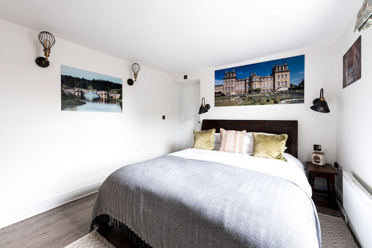 Quarto bem arrumado com uma cama grande, duas luminárias fixadas na parede e duas molduras com paisagens.