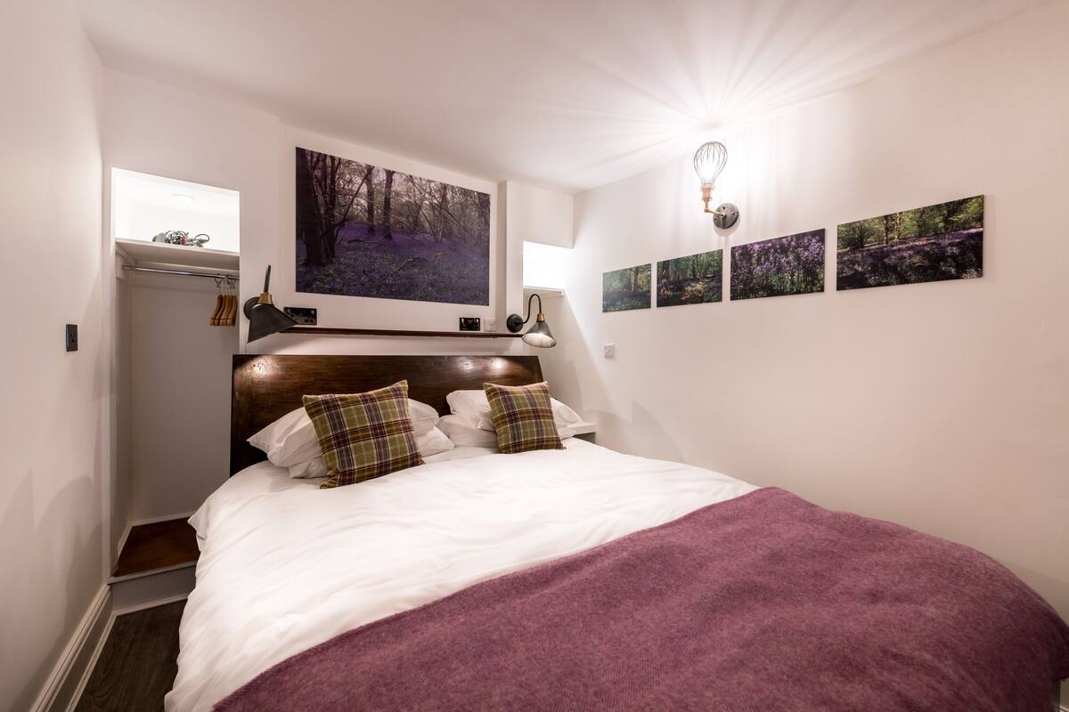 Cama bem arrumada com cabeceira, abajur e quadro na parede acima.