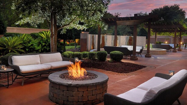 Un patio al aire libre con un hogar de piedra, sillones de descanso y una pérgola.