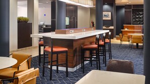 Zona de bar moderna con una barra central, taburetes y un área de estar con mesas y sillas.