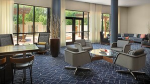 Un moderno vestíbulo de hotel con diversas opciones de asiento, incluyendo sofás y sillones, un comedor con mesa y sillas, y grandes ventanales que ofrecen vistas al exterior.