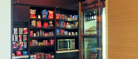 A small market area with shelves stocked with snacks and beverages, a microwave, and a refrigerator.