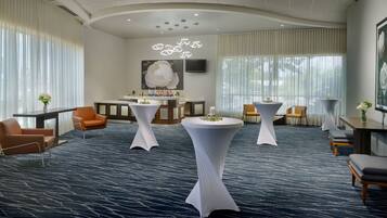 A hotel lobby with round tables, orange chairs, and a large white flower centerpiece.