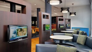 Un área de estar moderna con asientos y mesas, un televisor montado en la pared e iluminación decorativa.