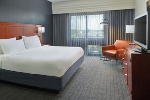 A hotel room with a large bed, a TV, a desk, and a view of the outdoors. - Courtyard by Marriott Warner Robins (Warner Robins)