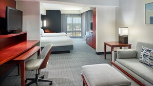 Habitación de hotel con cama, escritorio con computadora, televisor, sofá y una mesita de noche con lámpara.