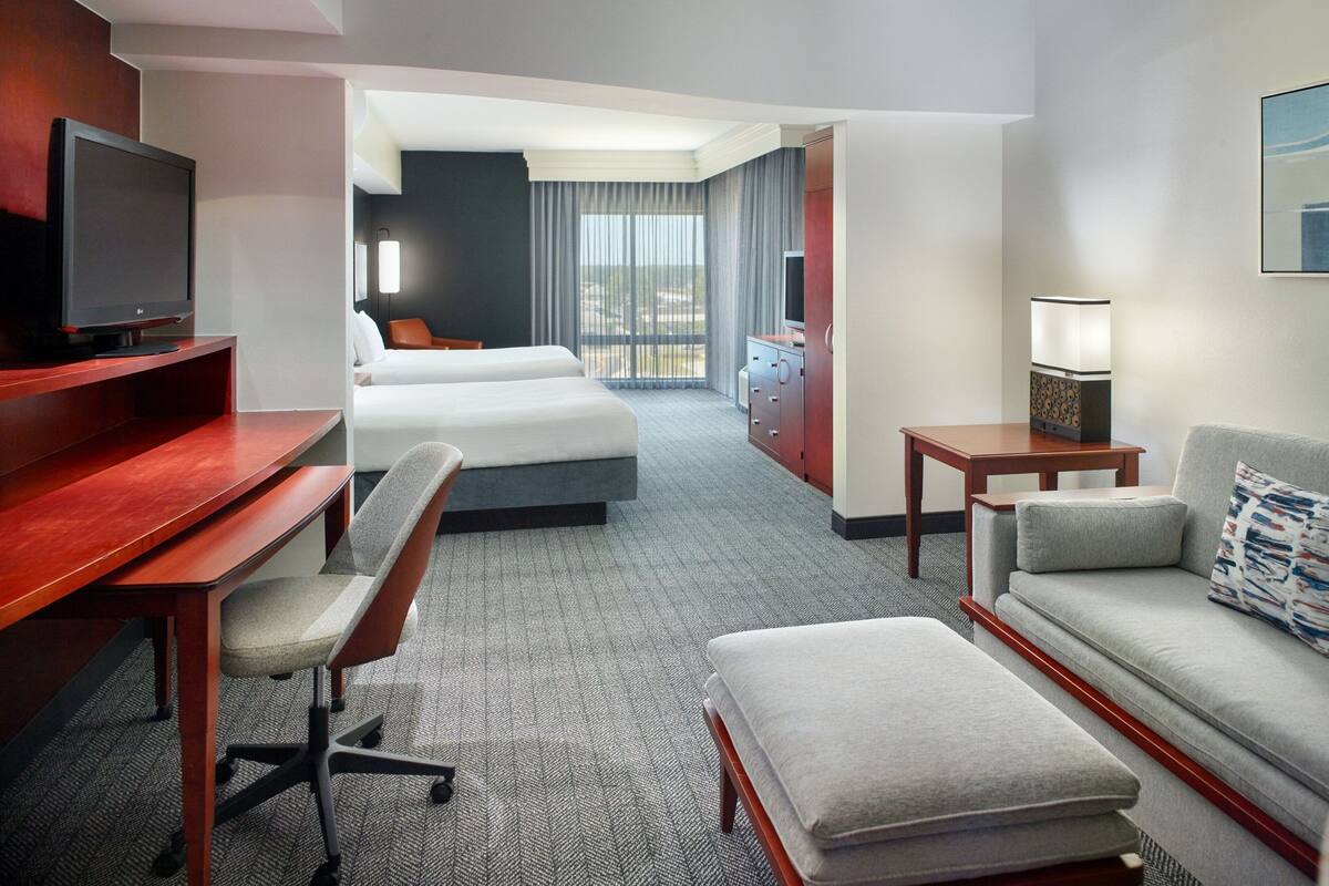 Habitación de hotel con cama, escritorio con computadora, televisor, sofá y una mesita de noche con lámpara.