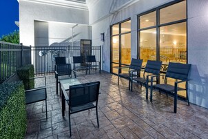Un área de estar al aire libre con mesas y sillas, un separador de vidrio y vistas al interior.