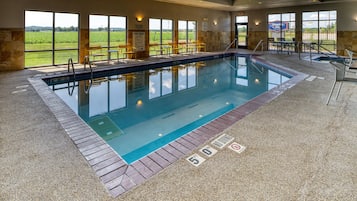 Una piscina interior con indicaciones claras de las normas de la piscina y carteles que prohíben el clavado, rodeada de muros de piedra y grandes ventanales.