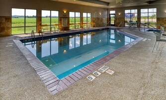 Una piscina interior con indicaciones claras de las normas de la piscina y carteles que prohíben el clavado, rodeada de muros de piedra y grandes ventanales.