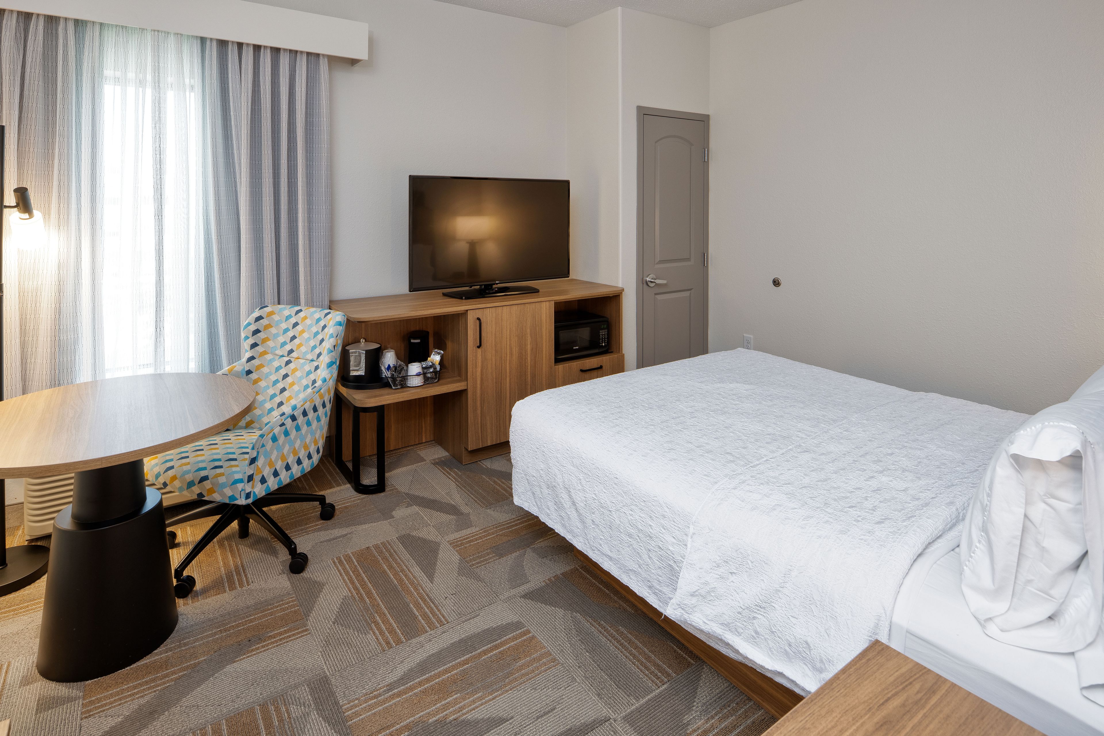 A hotel room with a bed, a desk with a computer, a chair, a television, and a door.