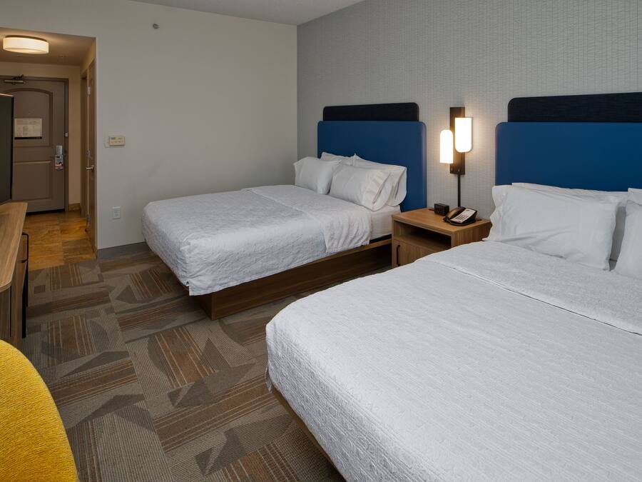 Habitación de hotel con dos camas, un escritorio, una silla, una mesita de noche con teléfono y una lámpara fijada a la pared.