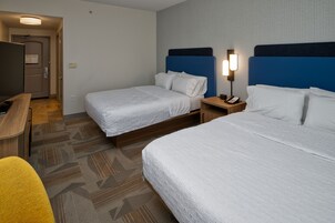 A hotel room with two beds, a desk, a chair, a nightstand with a phone, and a wall-mounted light fixture.
