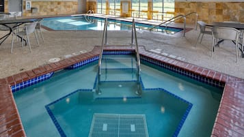 An indoor swimming pool with multiple lanes, safety railings, and a seating area with chairs.