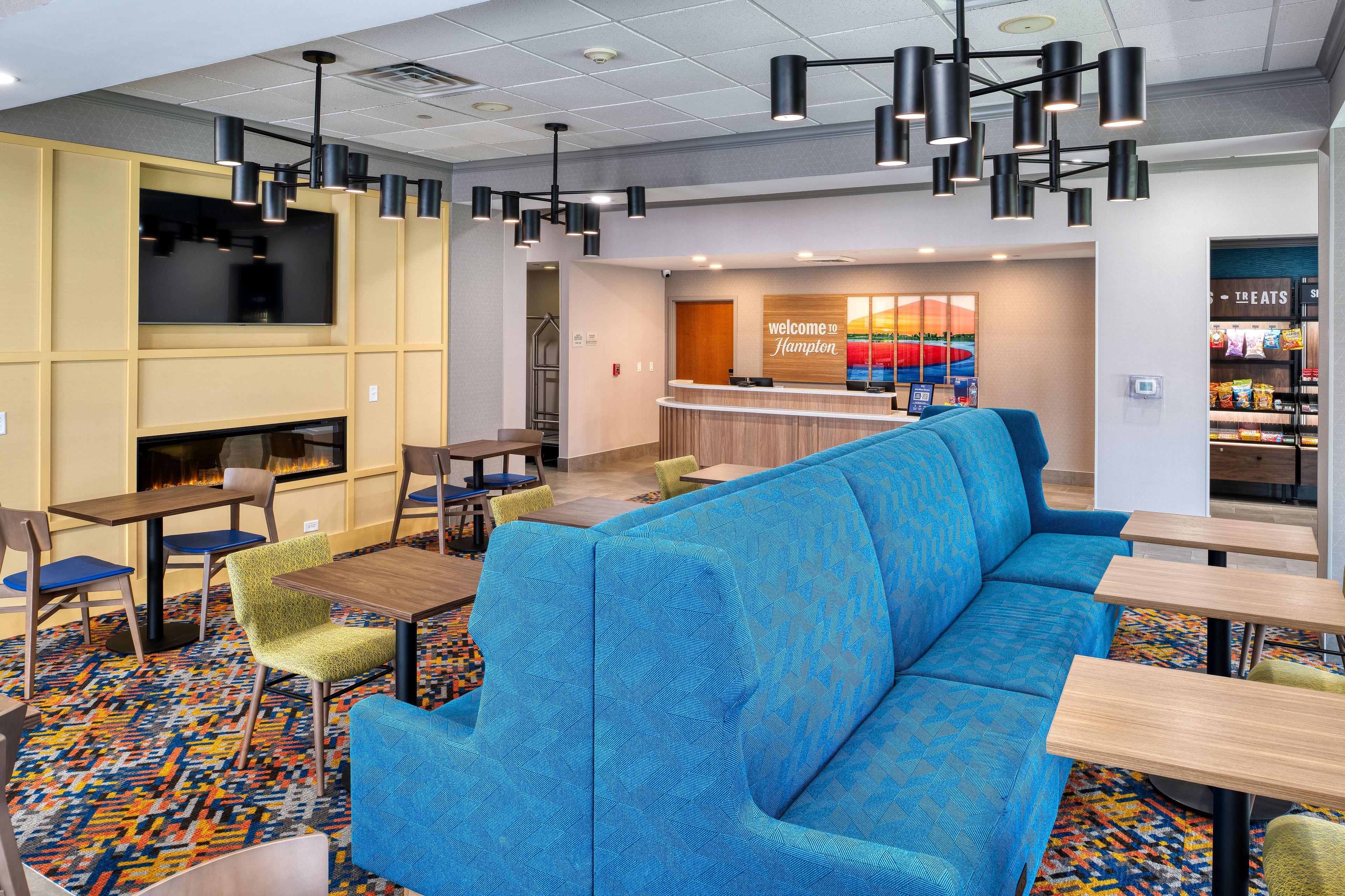 A hotel lobby with a reception desk, seating area, and a wall with a 'welcome to Hampton' sign.