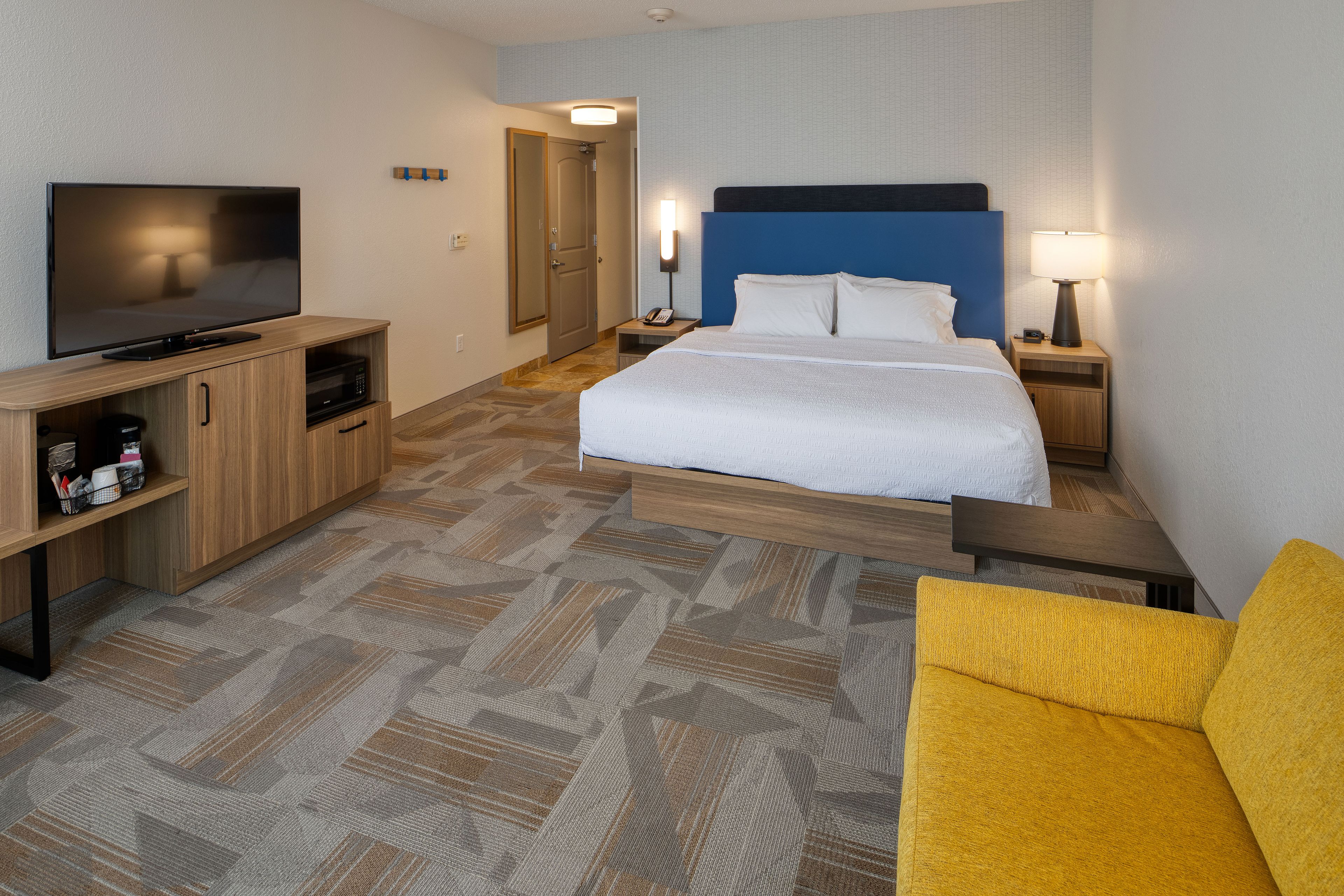 Una habitación de hotel con una cama, televisión, escritorio con lámpara y microondas.