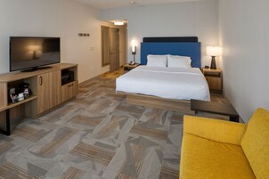 Una habitación de hotel con una cama, televisión, escritorio con lámpara y microondas.