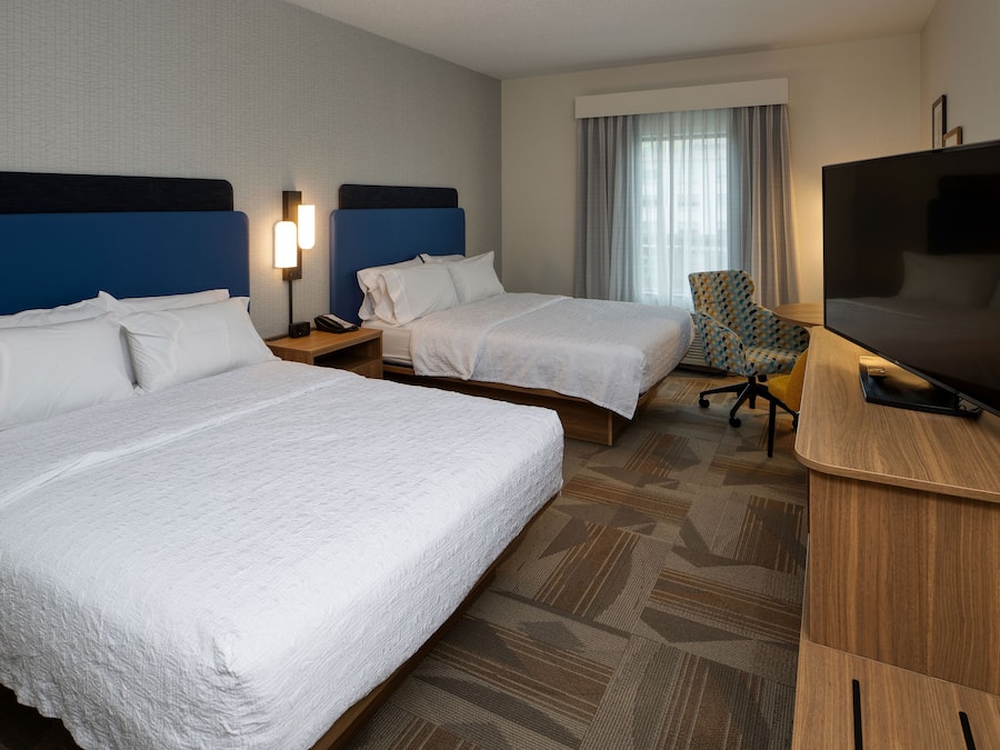 A hotel room with two beds, a television, a desk, and a chair.